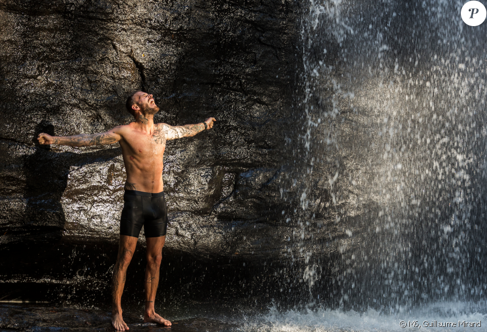 A person stands beneath a cascading waterfall