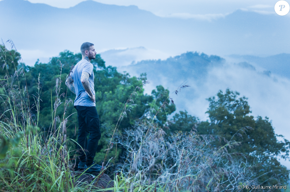 A person stands on a rocky outcrop, overlooking mist-shrouded mountains